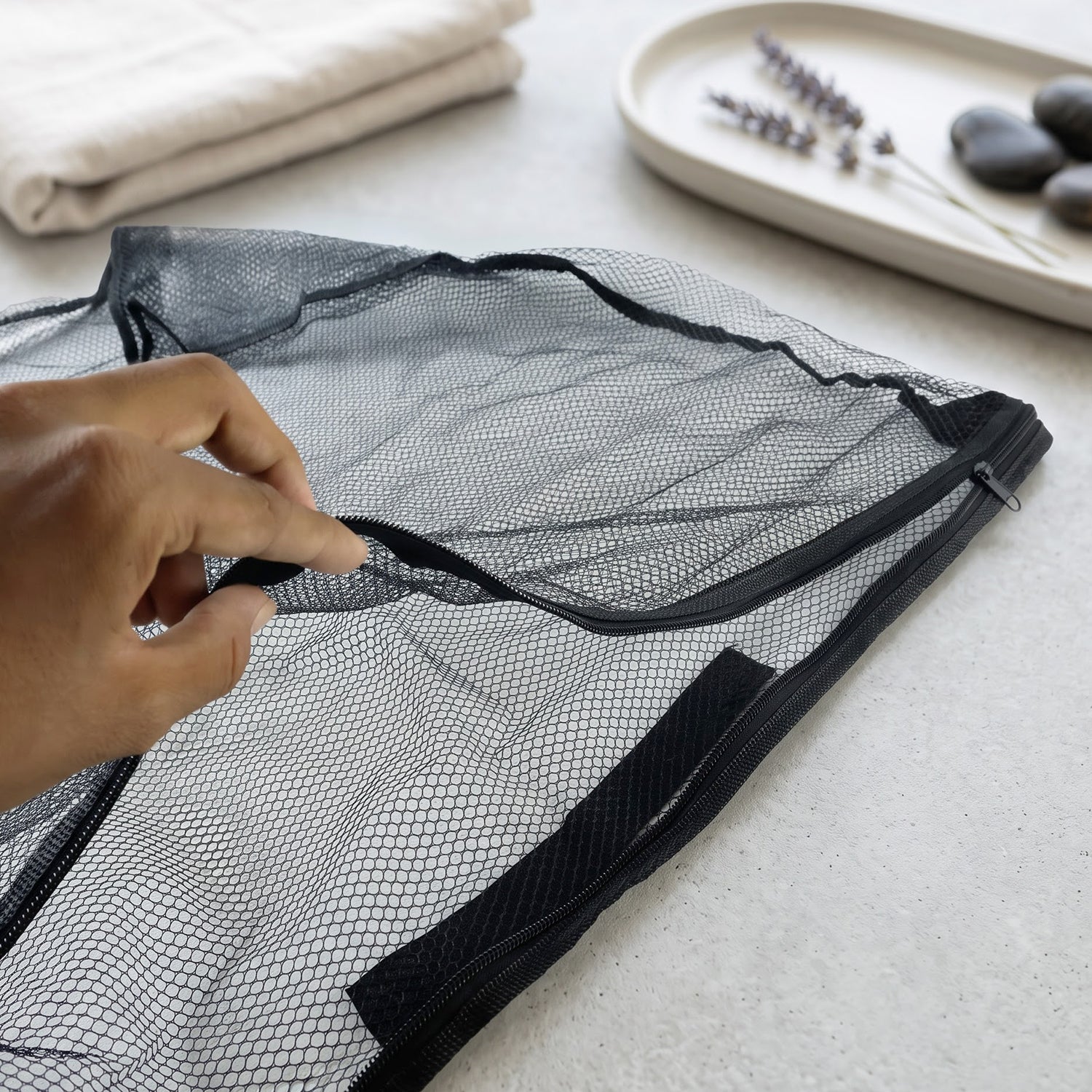 A hand unzips the top of a black mesh zipper bag on a light surface with spa items in the background.