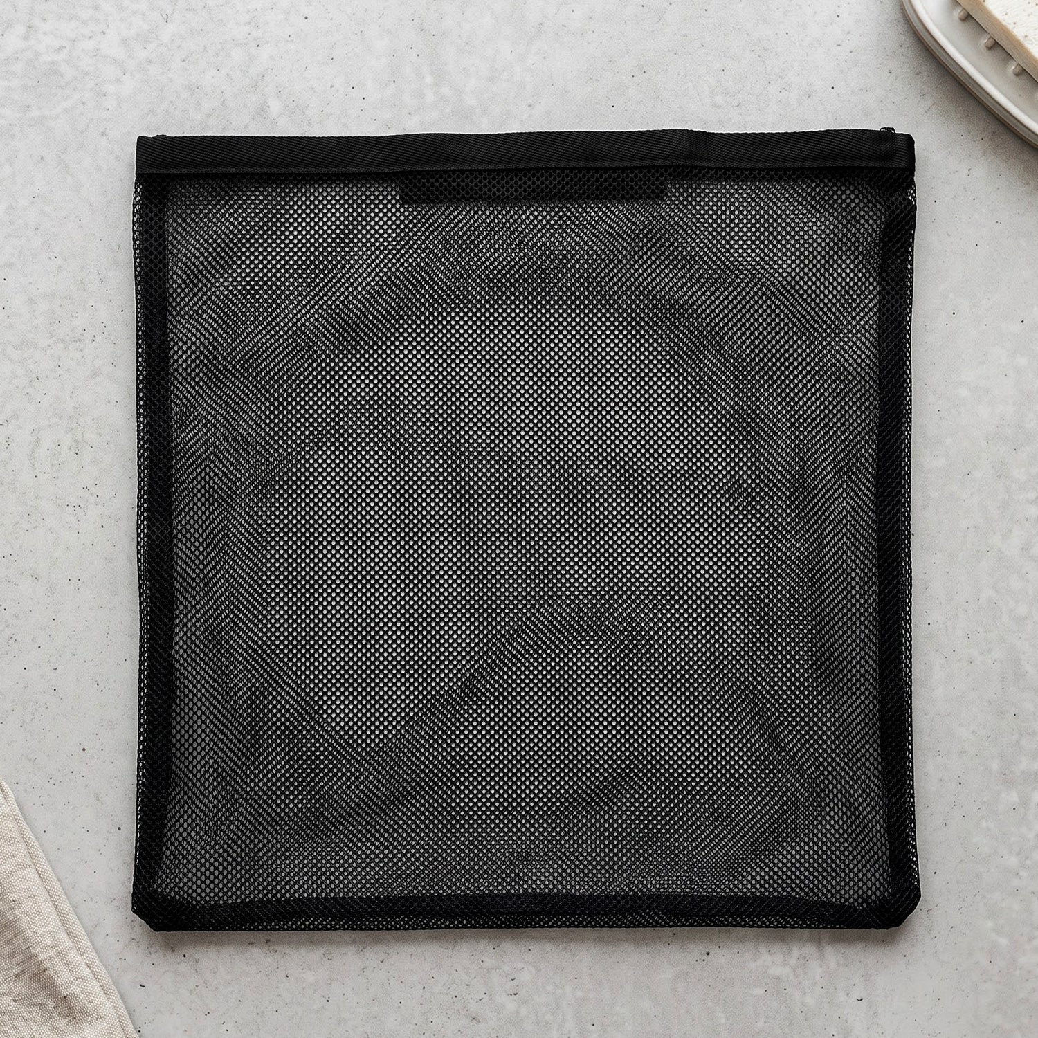 A flat black mesh zipper storage bag is laid out on a light grey textured surface.