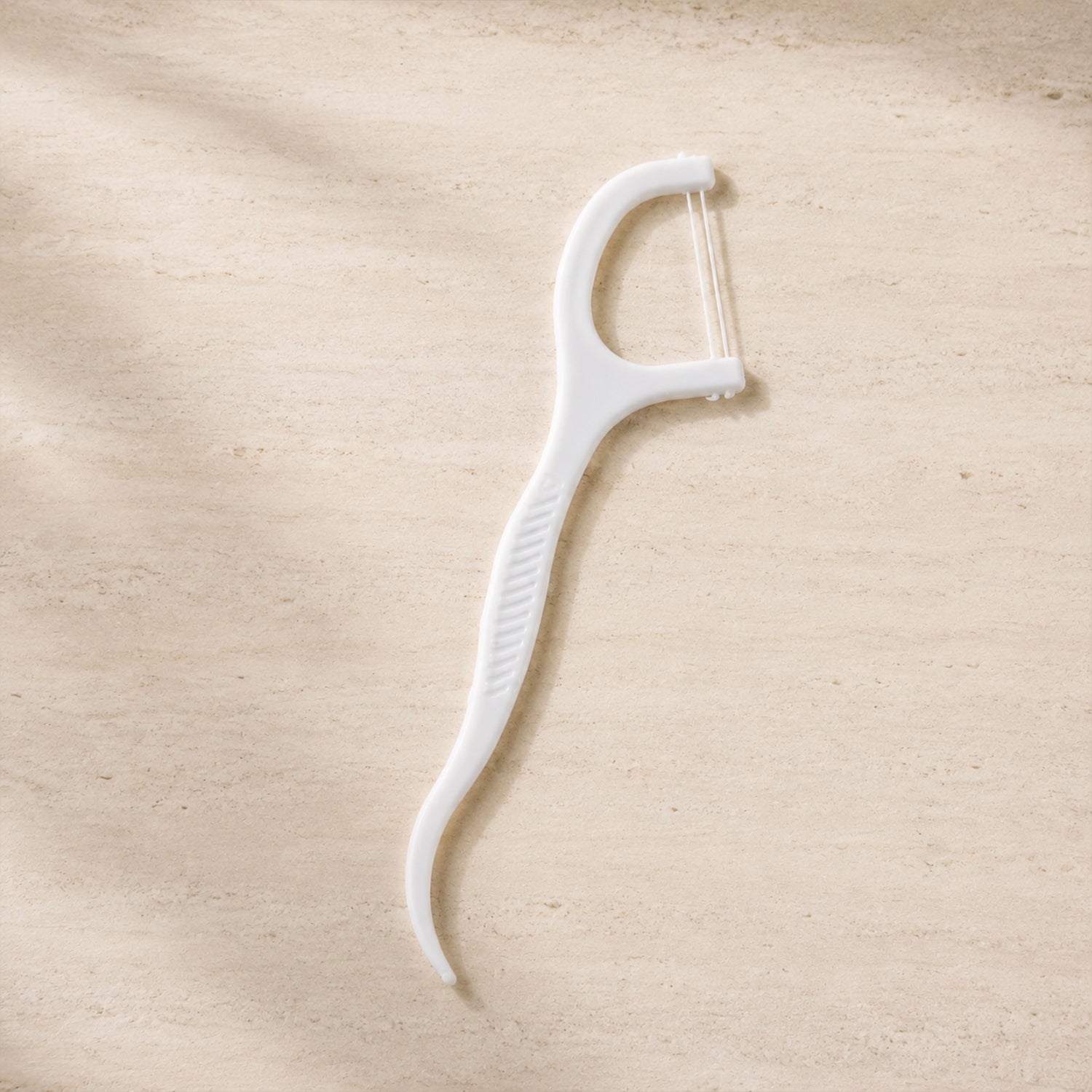 A single white dental floss pick with a textured handle lies on a light brown, textured surface.