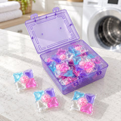 An open purple plastic storage box filled with colorful laundry detergent pods sits next to three loose pods. A washing