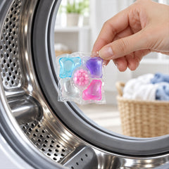 A hand holds a single multi-colored laundry pod, ready to place it into the open drum of a modern washing machine.