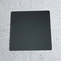 A square mirror with rounded corners lies flat on a speckled gray and white tiled floor.