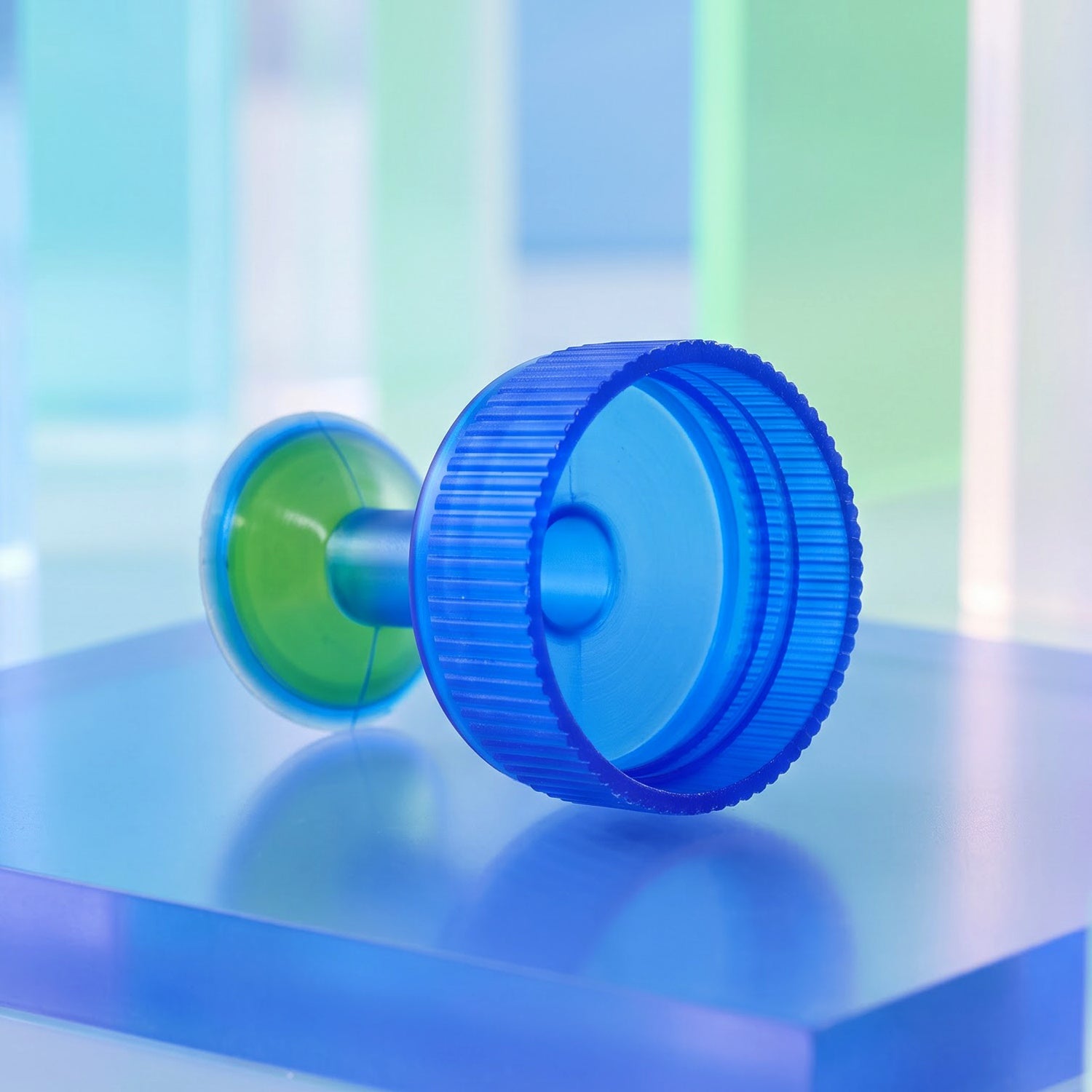The blue and green plastic sprinkler cap lies on its side on a blue translucent block, showing the threaded underside.