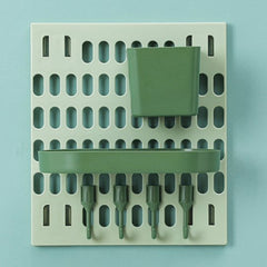 A light green pegboard with a dark green square cup and an oval tray, and four dark green hooks on a light blue background.