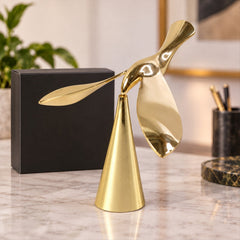 A shiny gold balancing bird sculpture with a conical base sits on a marble desk next to a black box.