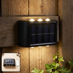 A black solar-powered LED wall light illuminates a wooden fence and green ivy at night, with an inset image of the light on