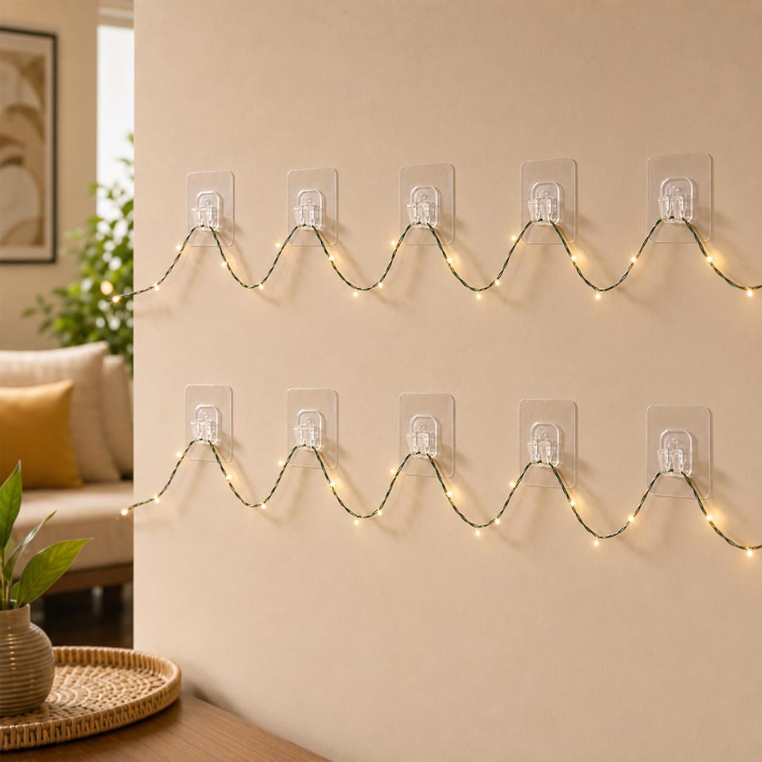 Two rows of clear adhesive hooks hold a string of illuminated fairy lights in a wavy pattern on a beige wall.