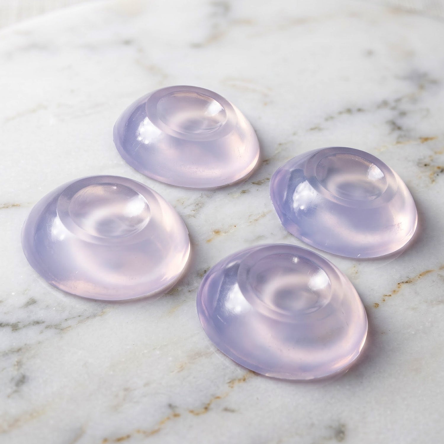 Four translucent, slightly purple-tinted silicone door stoppers are arranged on a white marble surface.