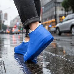 A person walks on a wet city street wearing blue silicone shoe covers over their shoes.