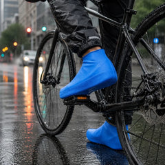 A person on a bicycle wears blue waterproof shoe covers on a wet city street