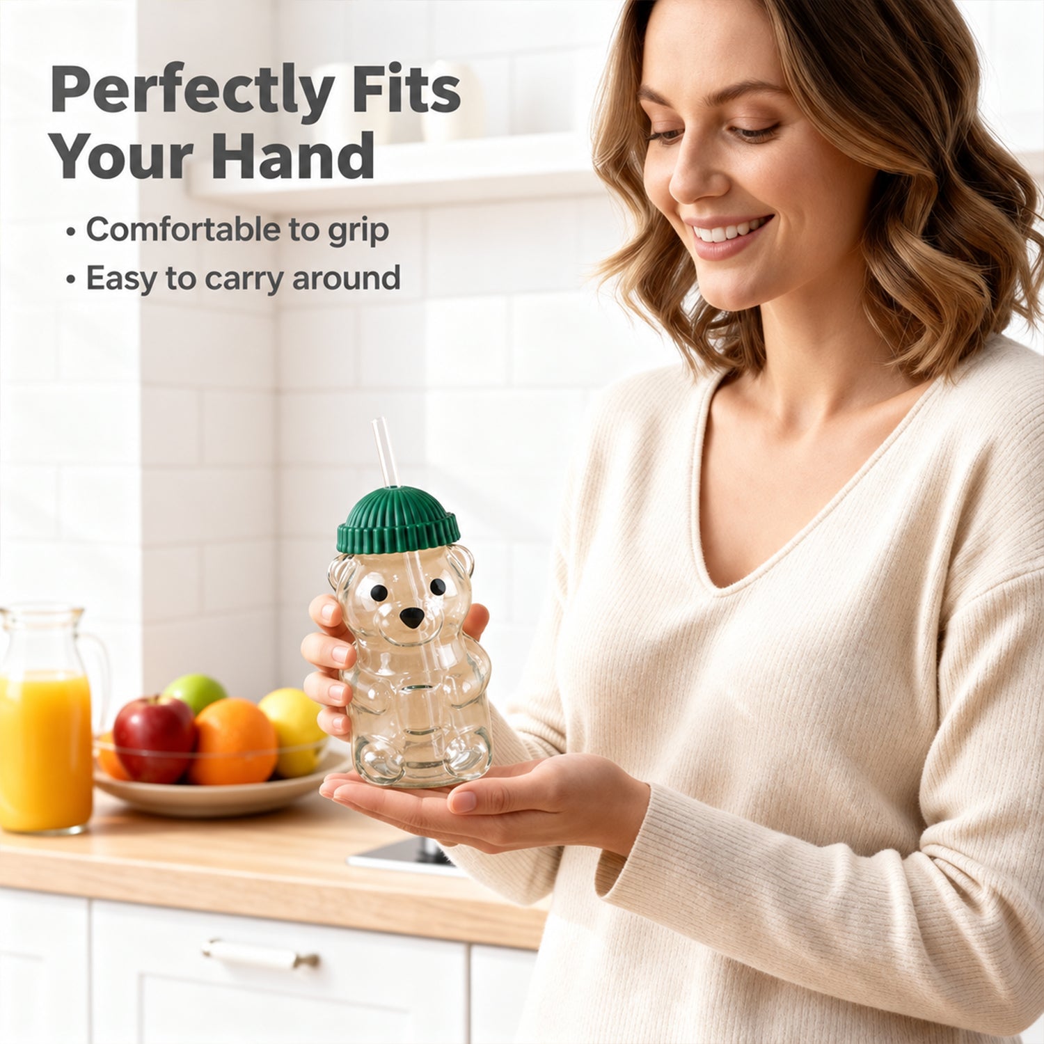 A smiling woman holds an empty bear-shaped glass sipper with a green lid, standing in a kitchen setting.