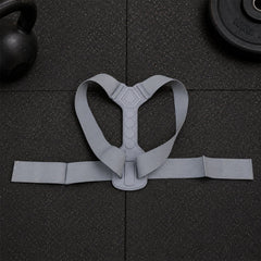 A grey posture corrector belt with a central spine support and shoulder straps laid flat on a dark textured surface.
