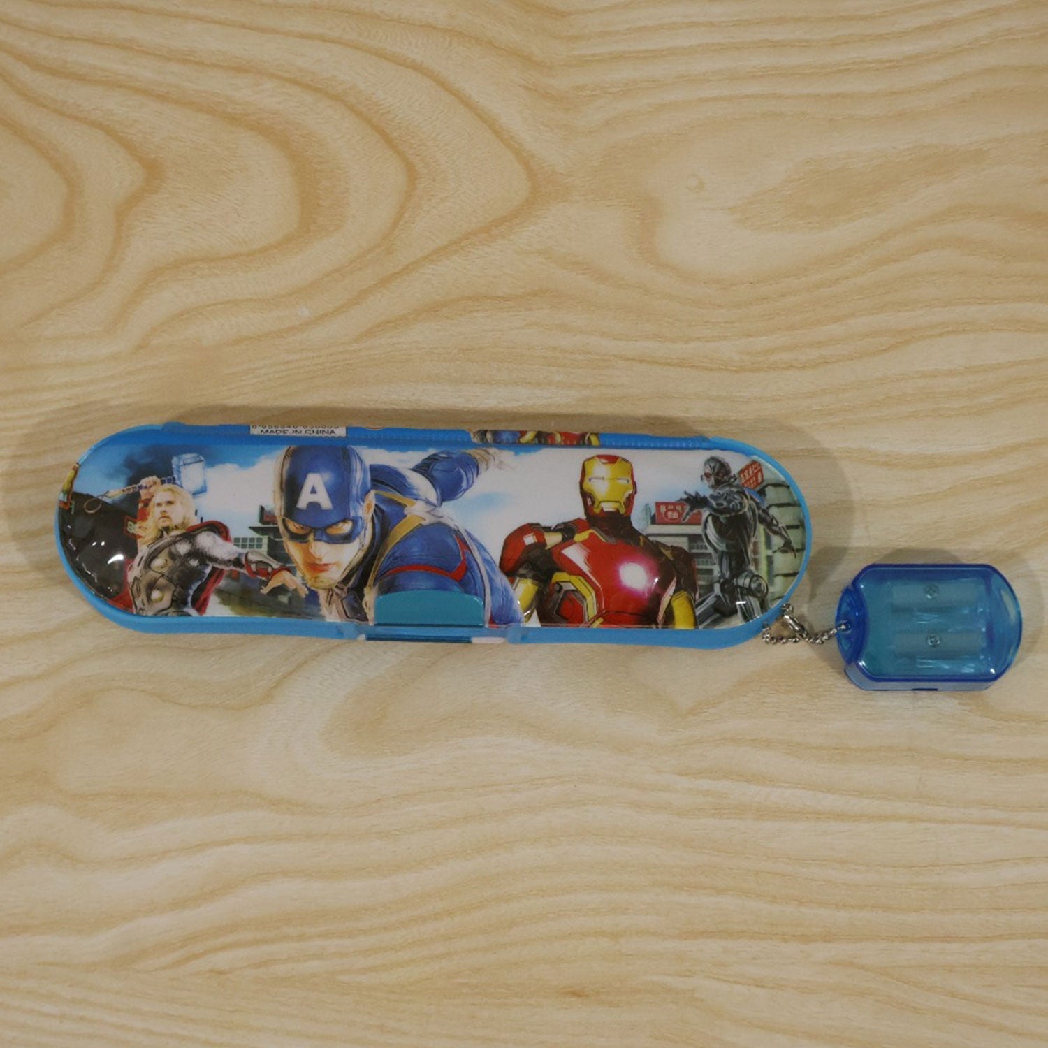 A blue Avengers pencil box with an attached sharpener resting on a light brown wooden surface.