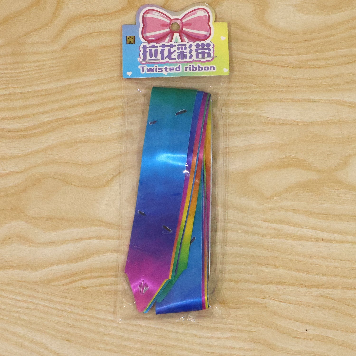 A single flat rainbow ribbon is sealed in clear plastic packaging with a colorful header card featuring a bow illustration