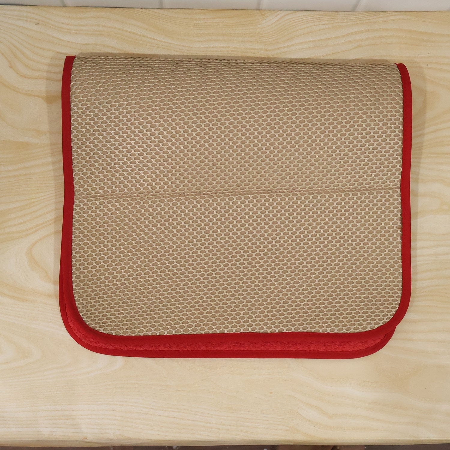 The beige mesh underside of a red rectangular bath mat is visible as it is folded in half on a light wooden surface.