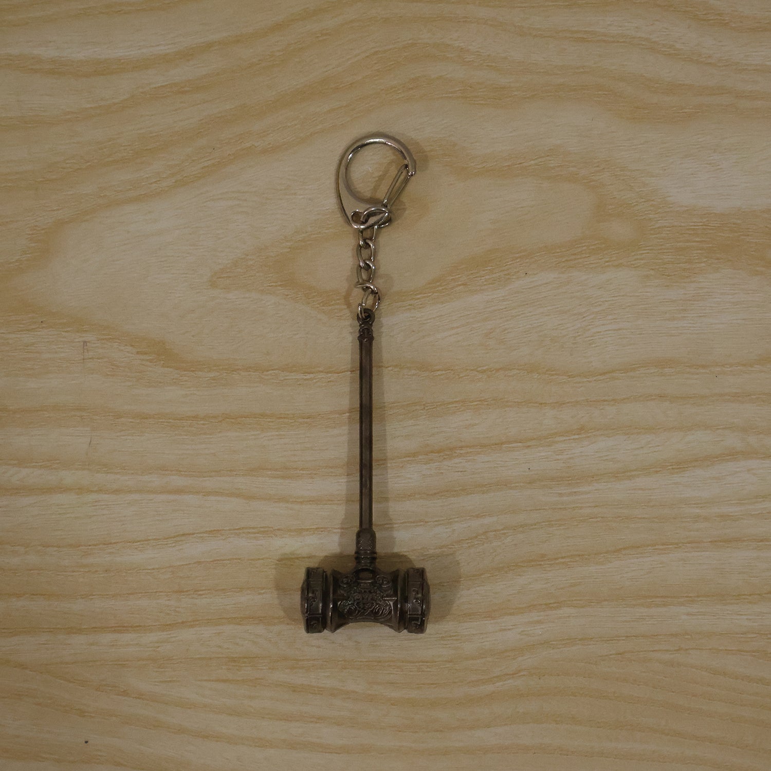The silver-plated hammer keychain with a clip ring, displayed flat on a light-colored wooden surface.