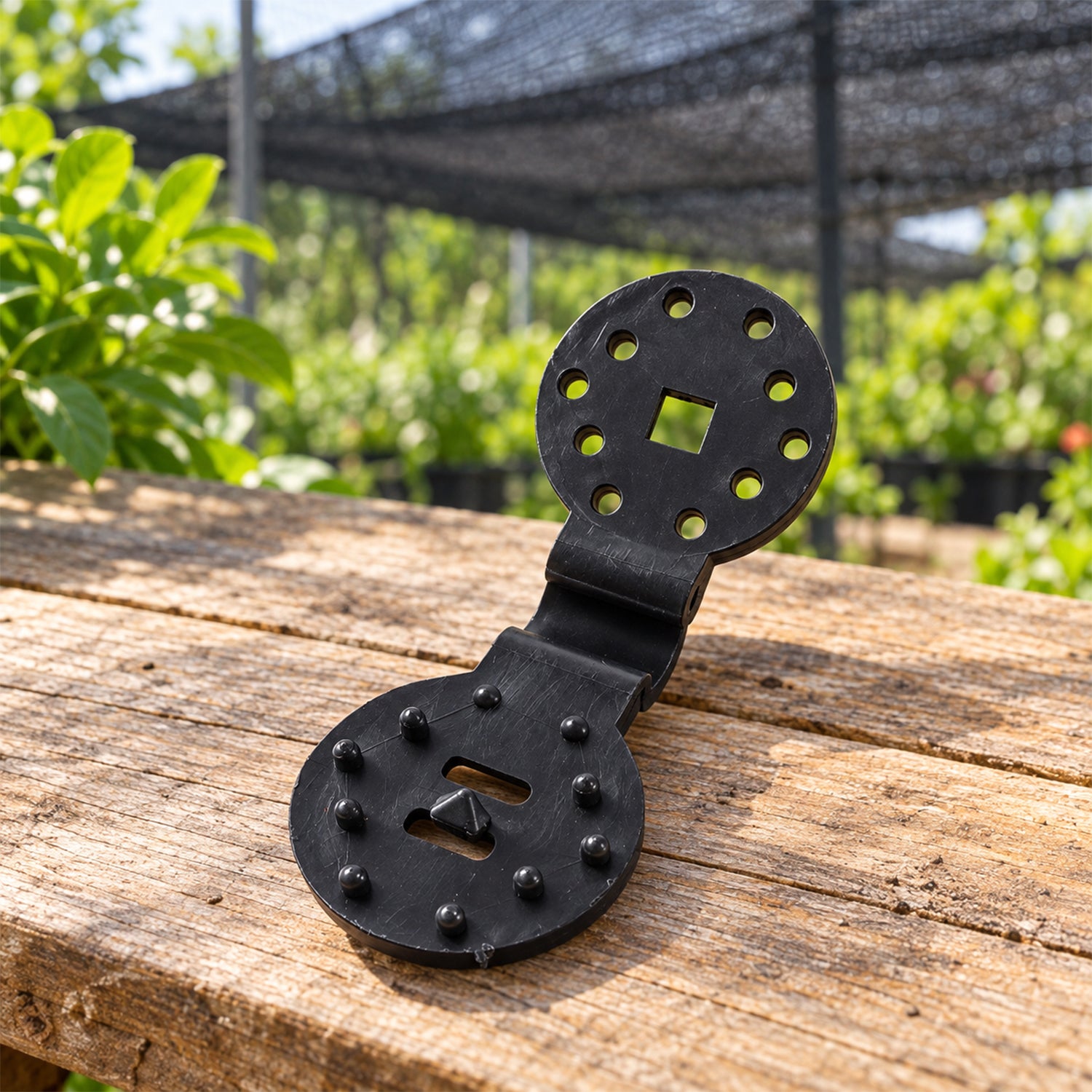 A single black plastic shade cloth clip with a hinged design, resting on a rustic wooden surface outdoors.