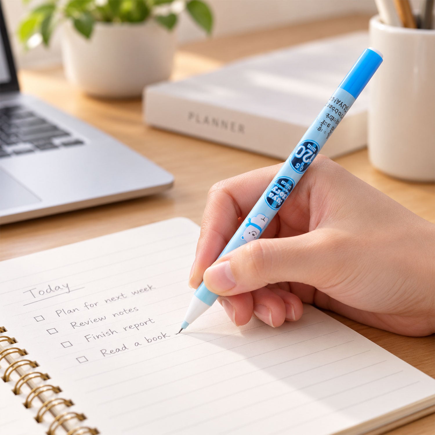 A hand writes a to-do list in a spiral notebook with a light blue mechanical pencil on a wooden desk.
