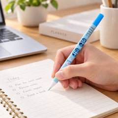 A hand writes a to-do list in a spiral notebook with a light blue mechanical pencil on a wooden desk.