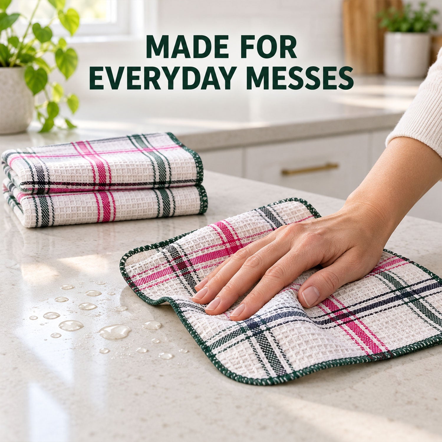 A hand wipes water droplets from a white counter with a white, pink, and green plaid dishcloth.