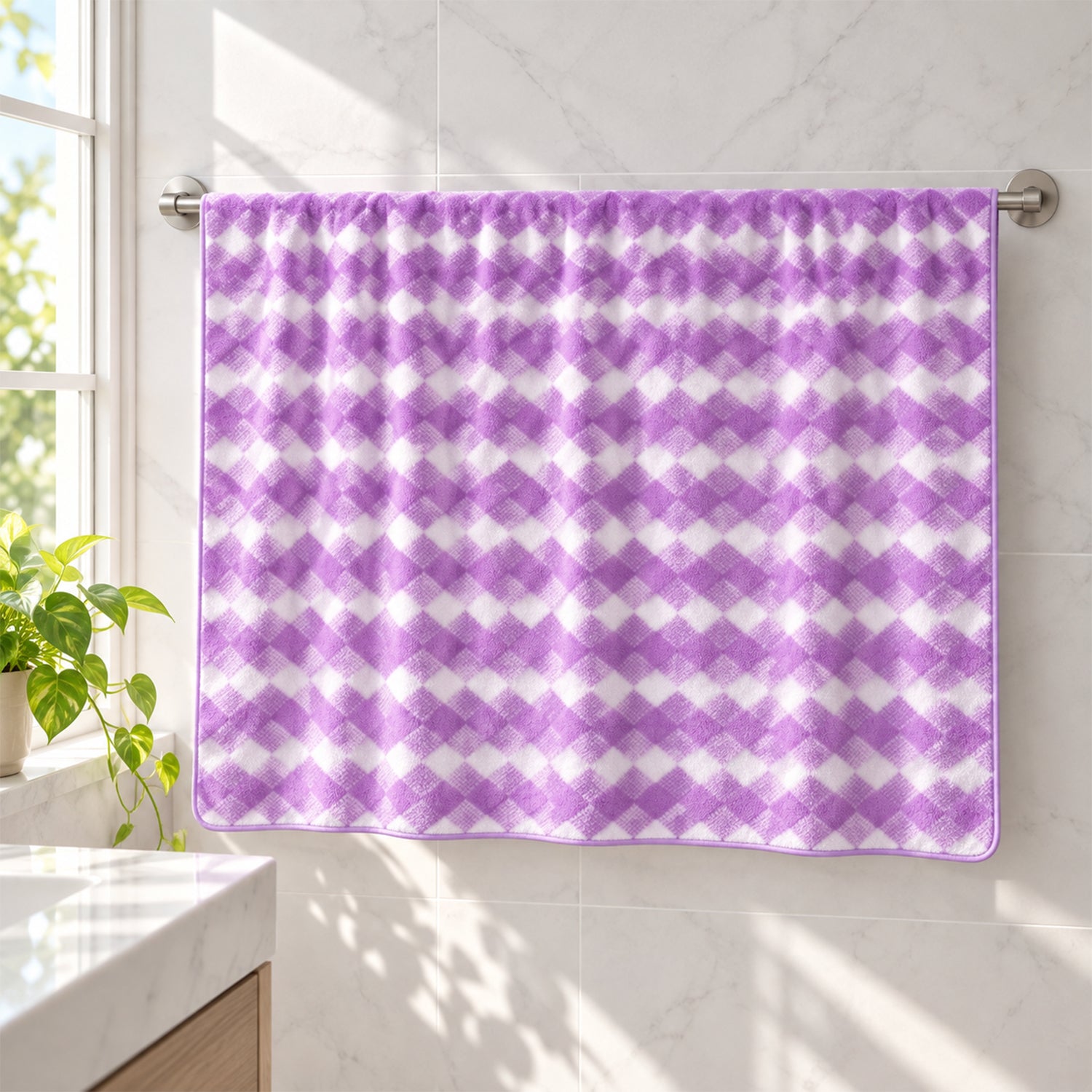 A purple and white checkered microfiber towel hanging neatly on a silver towel bar in a sunlit bathroom.