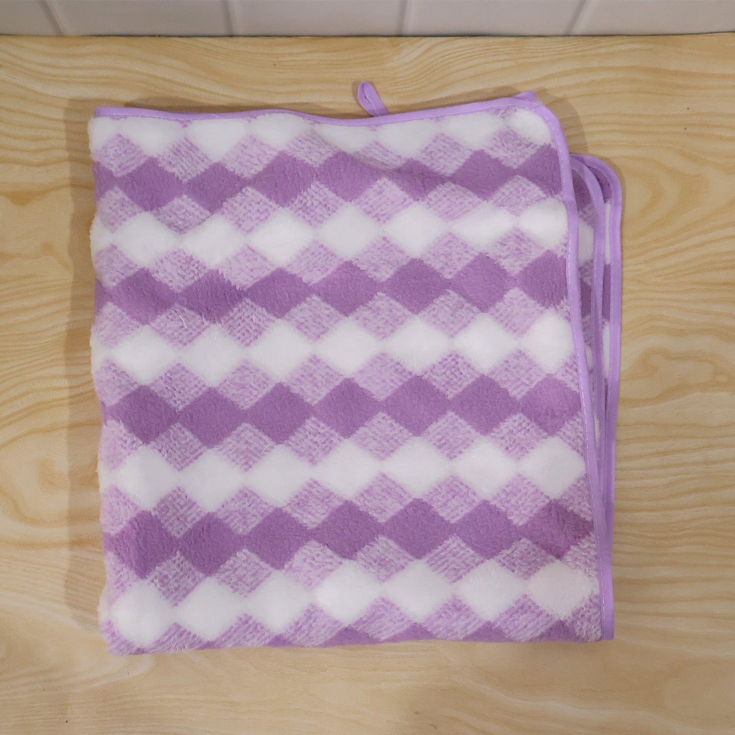 A purple and white checkered microfiber towel, folded, lying flat on a light wood surface.