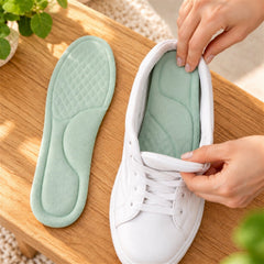 Hands inserting a light green insole into a white sneaker on a wooden surface, with another insole beside it.
