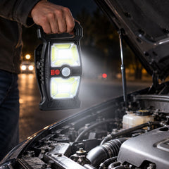 A person holds a black solar motion sensor clip light over an open car engine at night, illuminating the components.