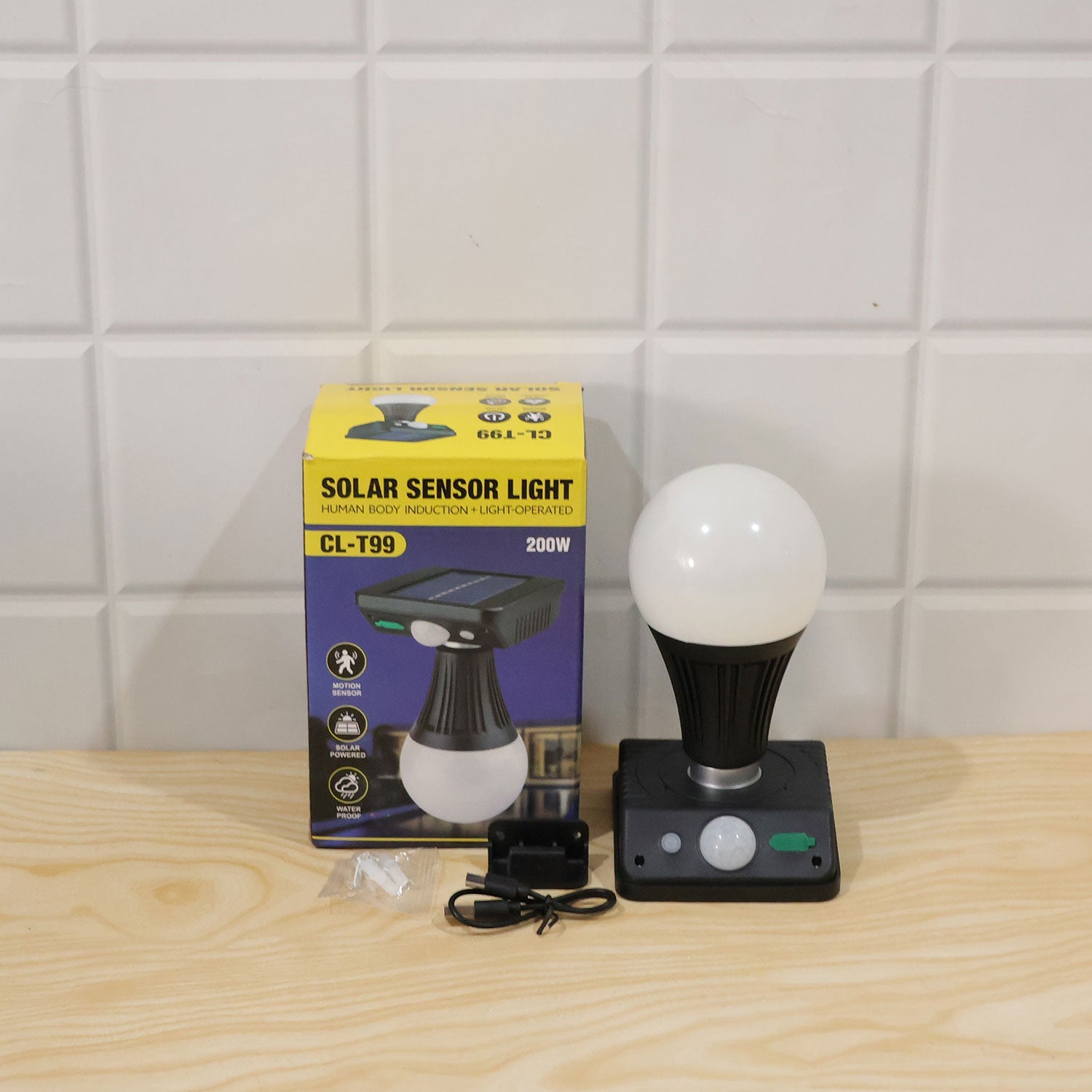 A black solar light with a white globe bulb, its product box, and charging accessories on a wooden surface.
