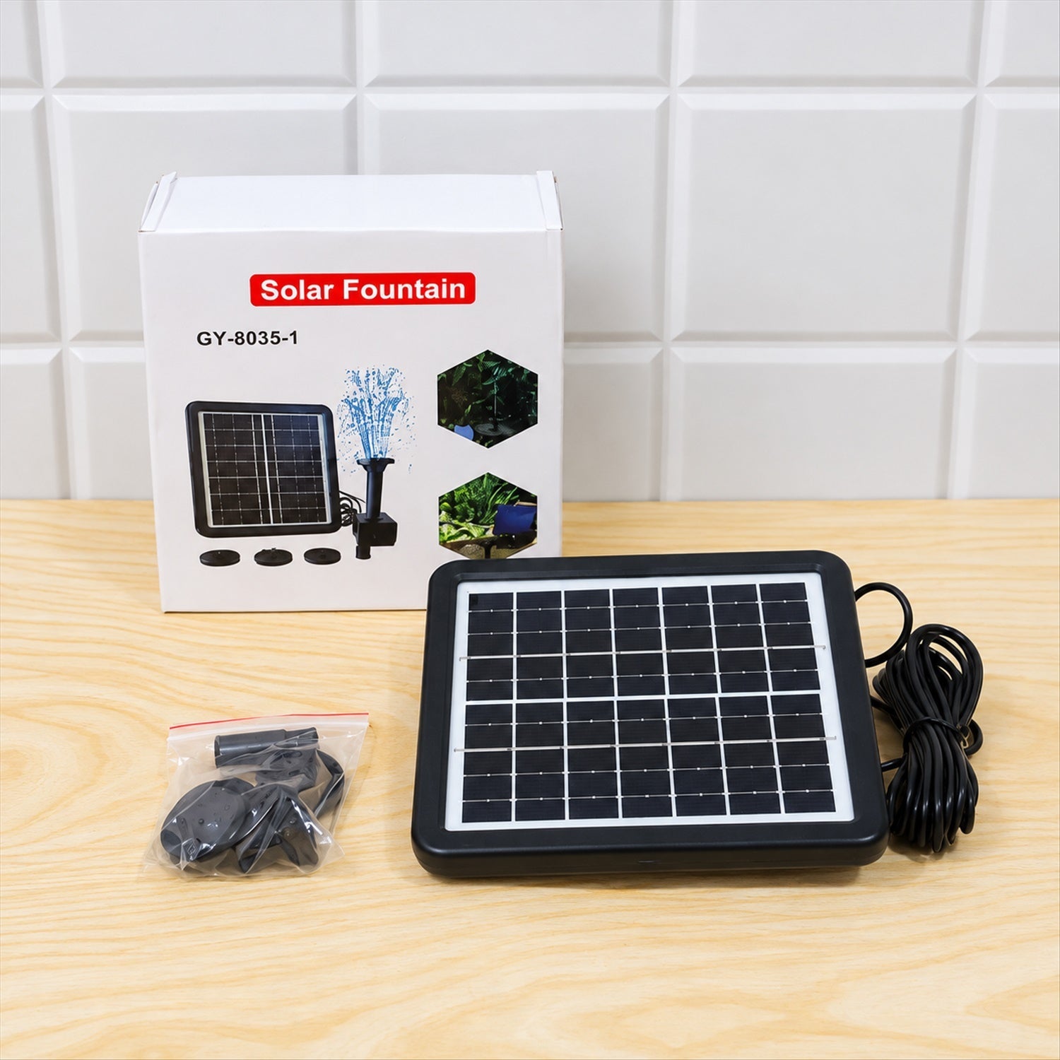 A black solar panel, pump, and small bag of parts are shown on a wooden surface next to the product box.