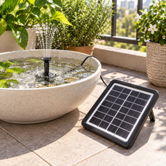 A solar panel and pump create a small fountain in a light-colored bowl on a patio with potted plants.