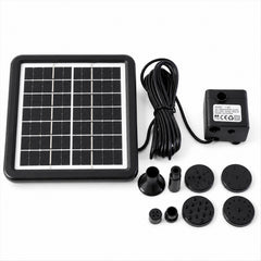 A black solar panel, pump, coiled wire, and multiple fountain nozzles are neatly arranged on a white surface.