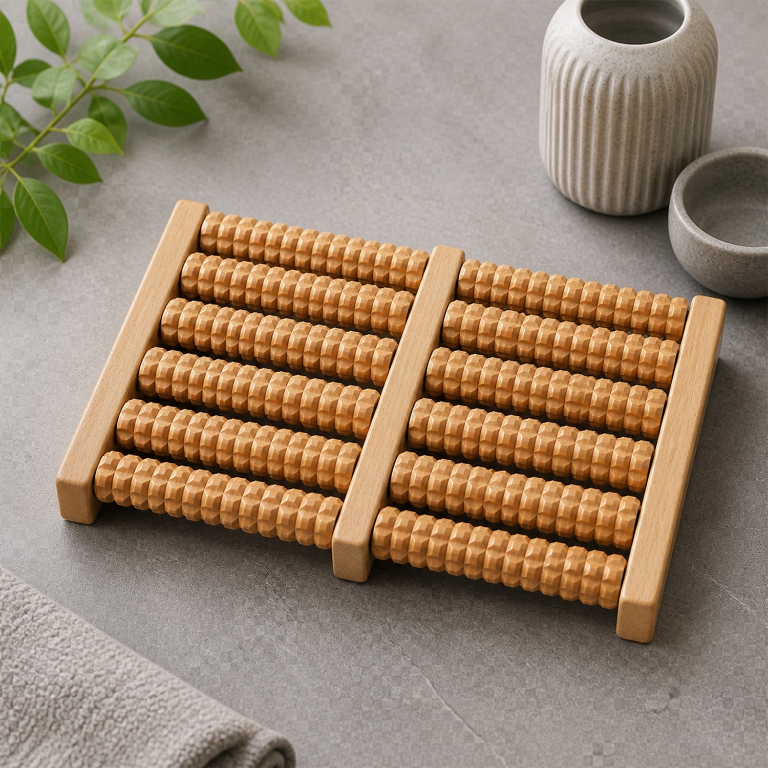 A light brown wooden foot massager with textured rollers on a grey surface, next to a grey towel and ceramic vases.
