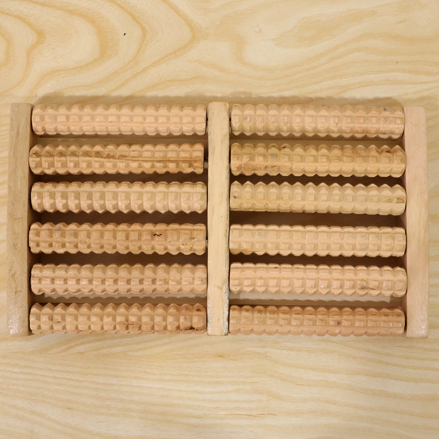 A light brown wooden foot massager with ten textured rollers, viewed from above on a light wood grain surface.