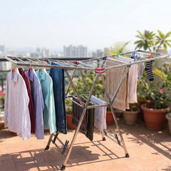 A silver clothes drying rack holding various garments, positioned on a sunny outdoor balcony with potted plants.
