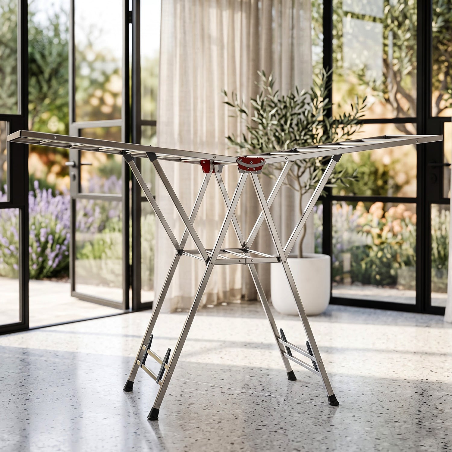 A shiny metal clothes drying rack with red plastic details, positioned indoors on a tiled floor with large glass doors.