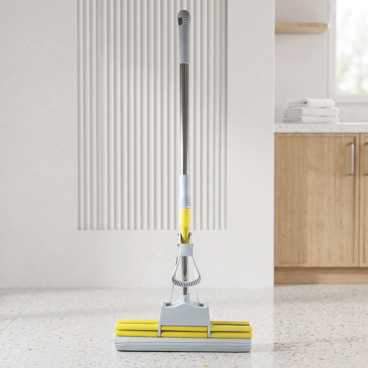 A yellow and grey sponge mop stands upright on a speckled floor in a modern room with wooden cabinets.