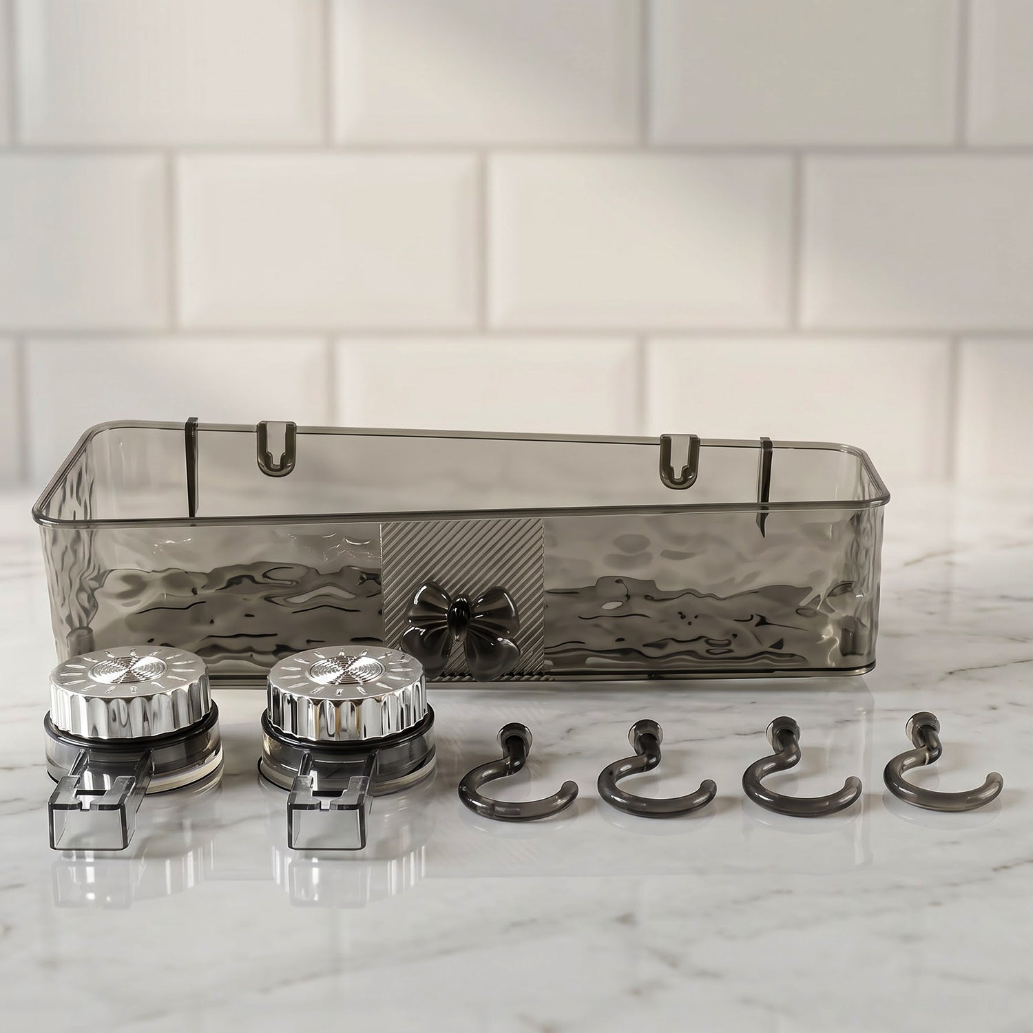 A clear grey plastic caddy, two silver suction cups, and four grey hooks are arranged on a white marble surface.