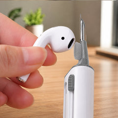 A hand holding a white earbud while the cleaning pen's small brush cleans the earbud speaker.