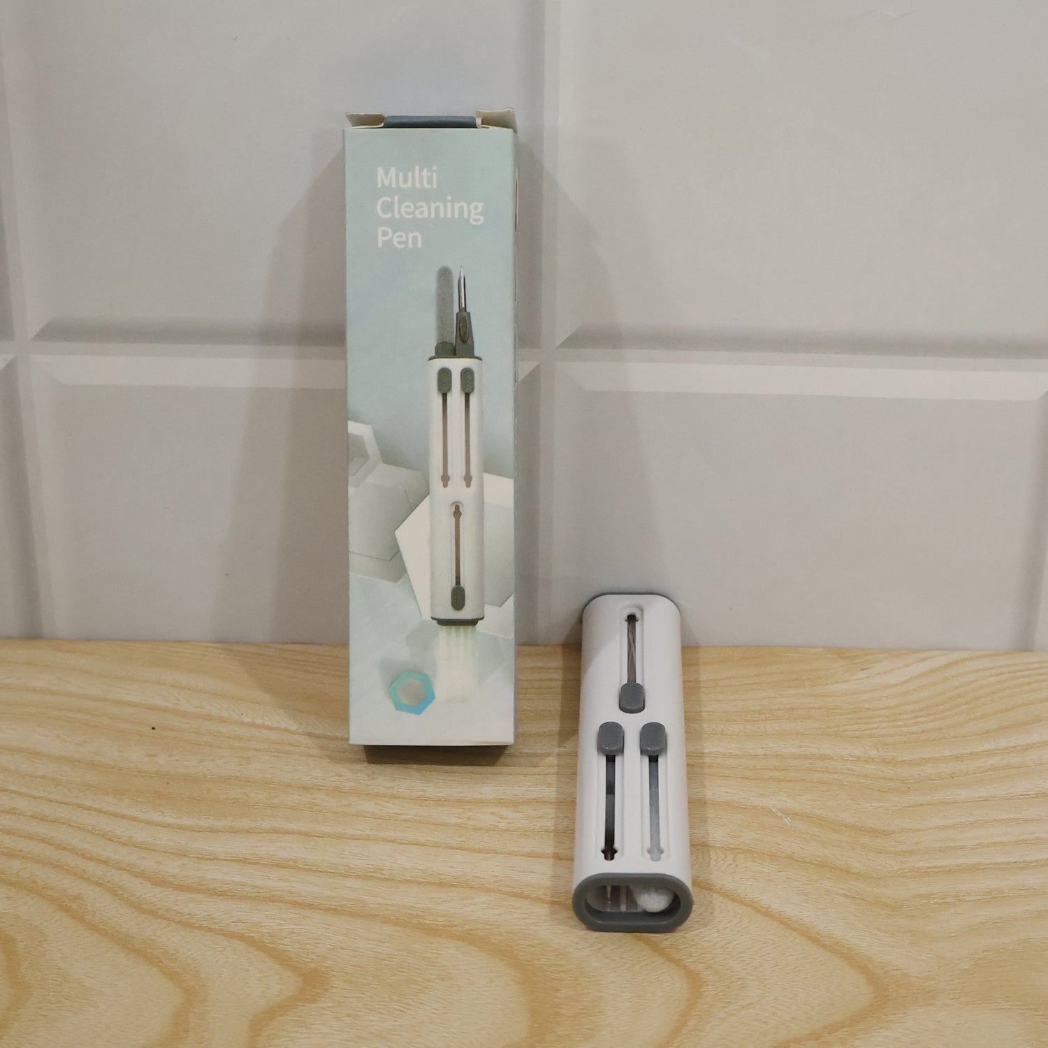 The multi-tool cleaning pen next to its light blue and white retail packaging on a wooden surface.