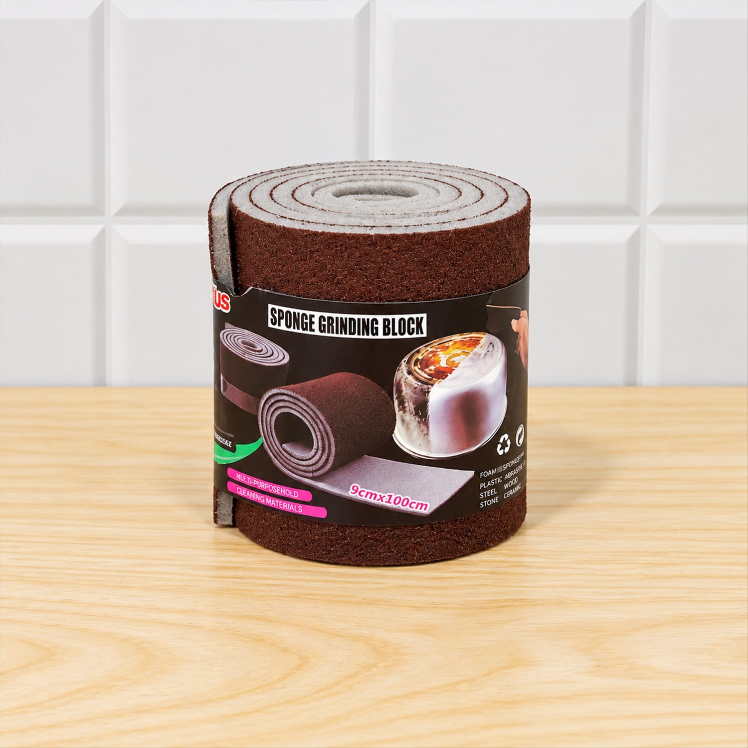A rolled-up brown abrasive sponge with a label, standing on a light wooden table against white tiled wall.