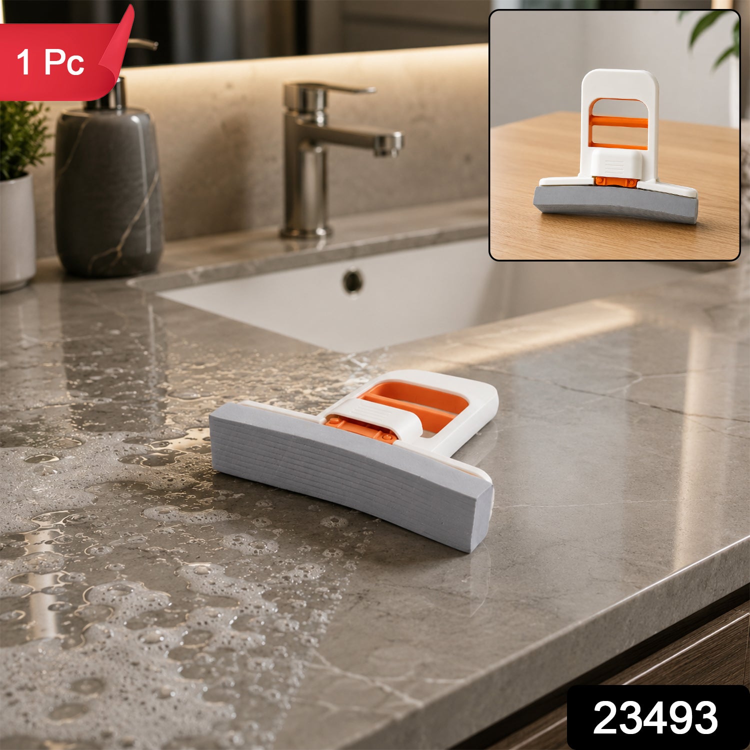 A white and orange mini sponge mop with a grey sponge head sits on a light wooden table, with a green plant in the