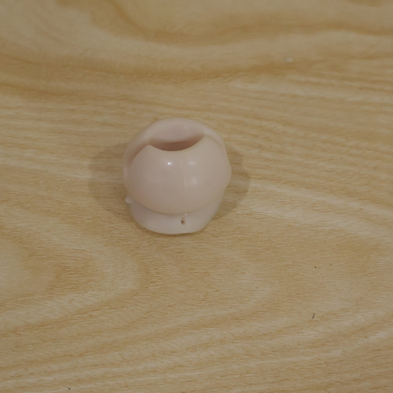 A single white toothbrush holder clip resting on a light brown wooden surface.