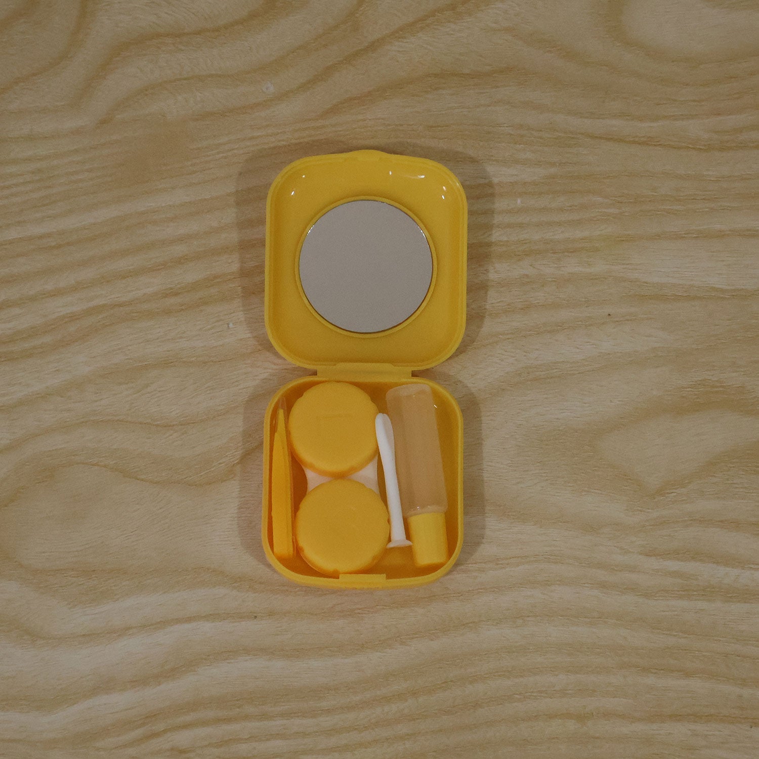 A yellow contact lens case, open to reveal a mirror, two lens holders, a solution bottle, tweezers, and an applicator on a