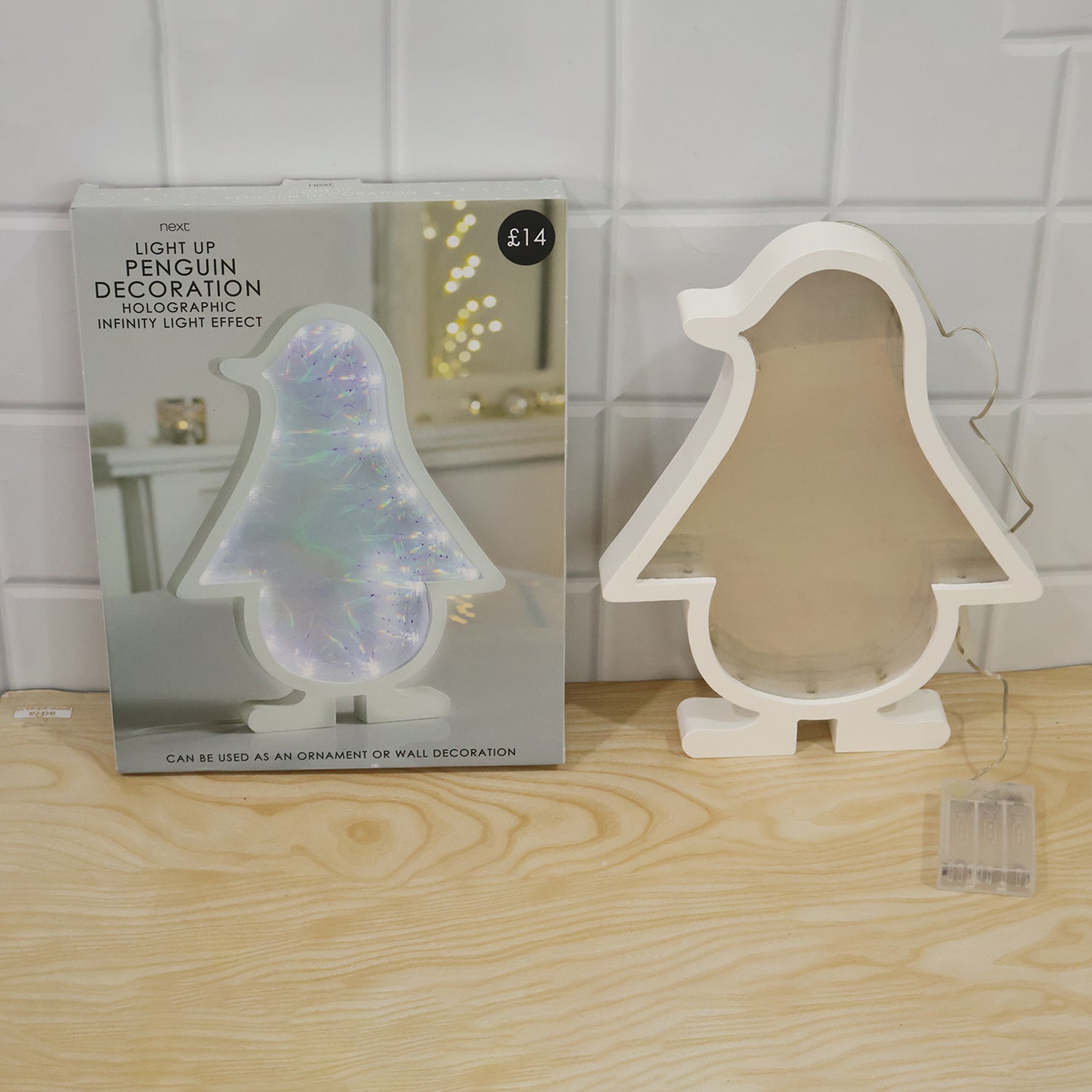 White penguin-shaped infinity mirror light unlit next to its product packaging, both on a light wooden surface.