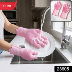 Hands wearing pink silicone gloves with scrubbing bristles washing a white plate under running water in a kitchen sink, with
