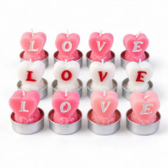Twelve unlit heart-shaped tealight candles, pink and white, spelling LOVE, arranged in rows on a white surface.