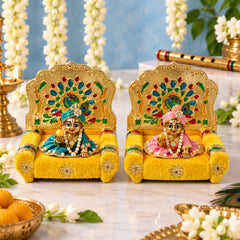 Two ornate golden singhasans with yellow velvet seats, each featuring a colorful peacock design on the backrest, with two
