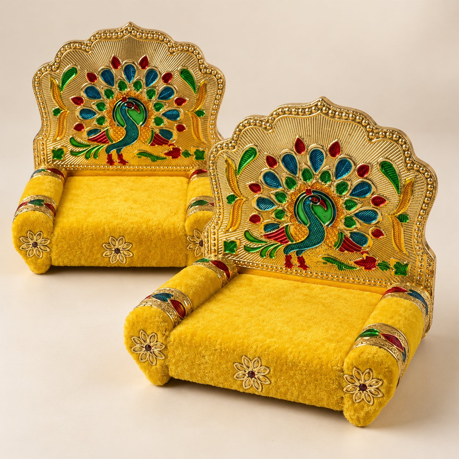 A slightly angled view of two golden singhasans with yellow velvet seats and detailed peacock backrests on a light surface.