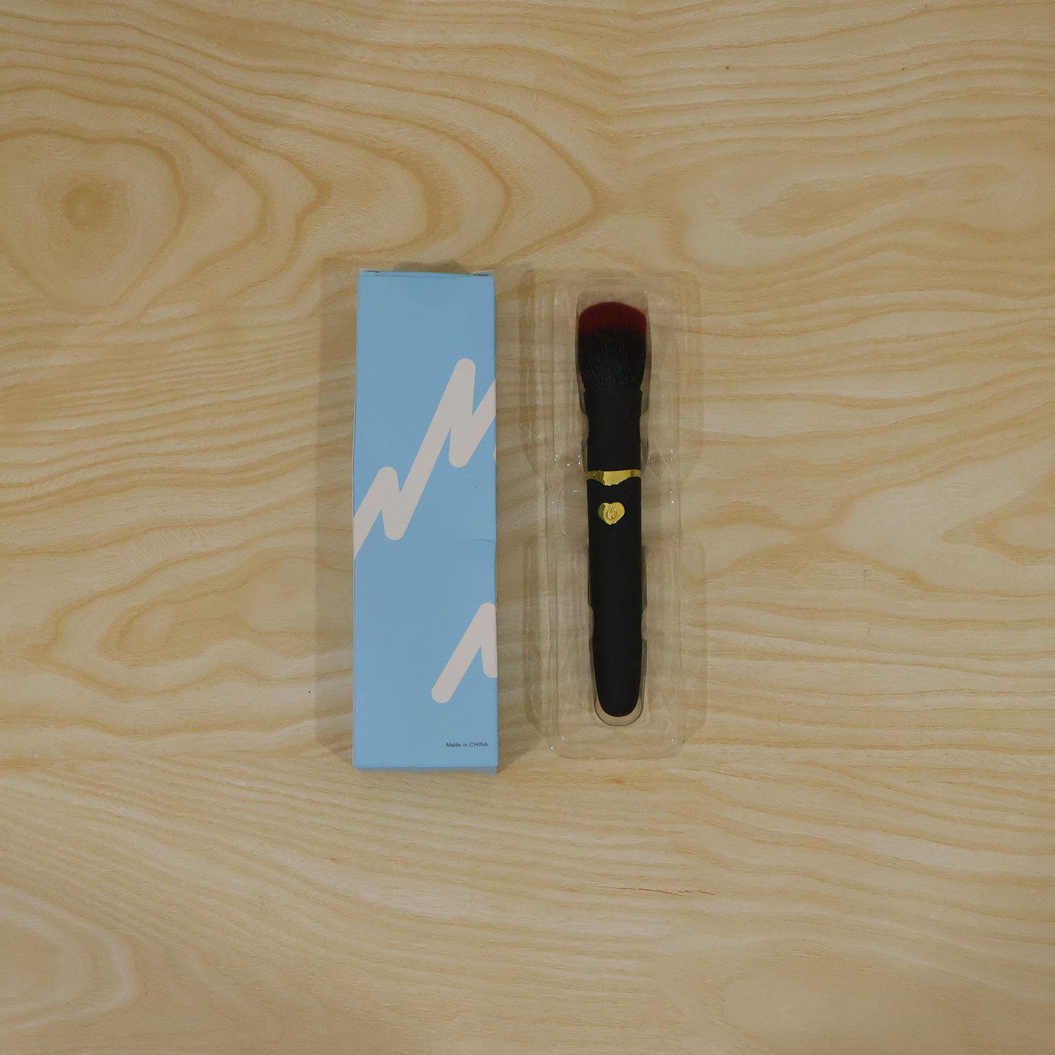 A black and red makeup brush with gold accents is used by a woman to apply blush to her cheek, with a USB port detail.